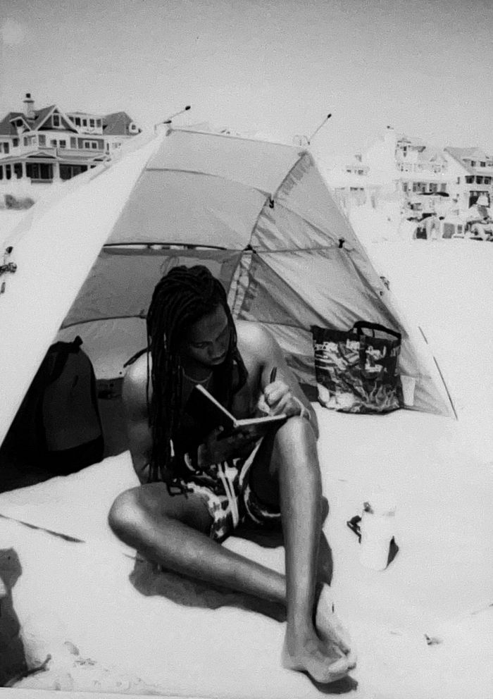 Polaroid of Roth$child on the beach, sitting in front of a small tent and writing in a notebook.