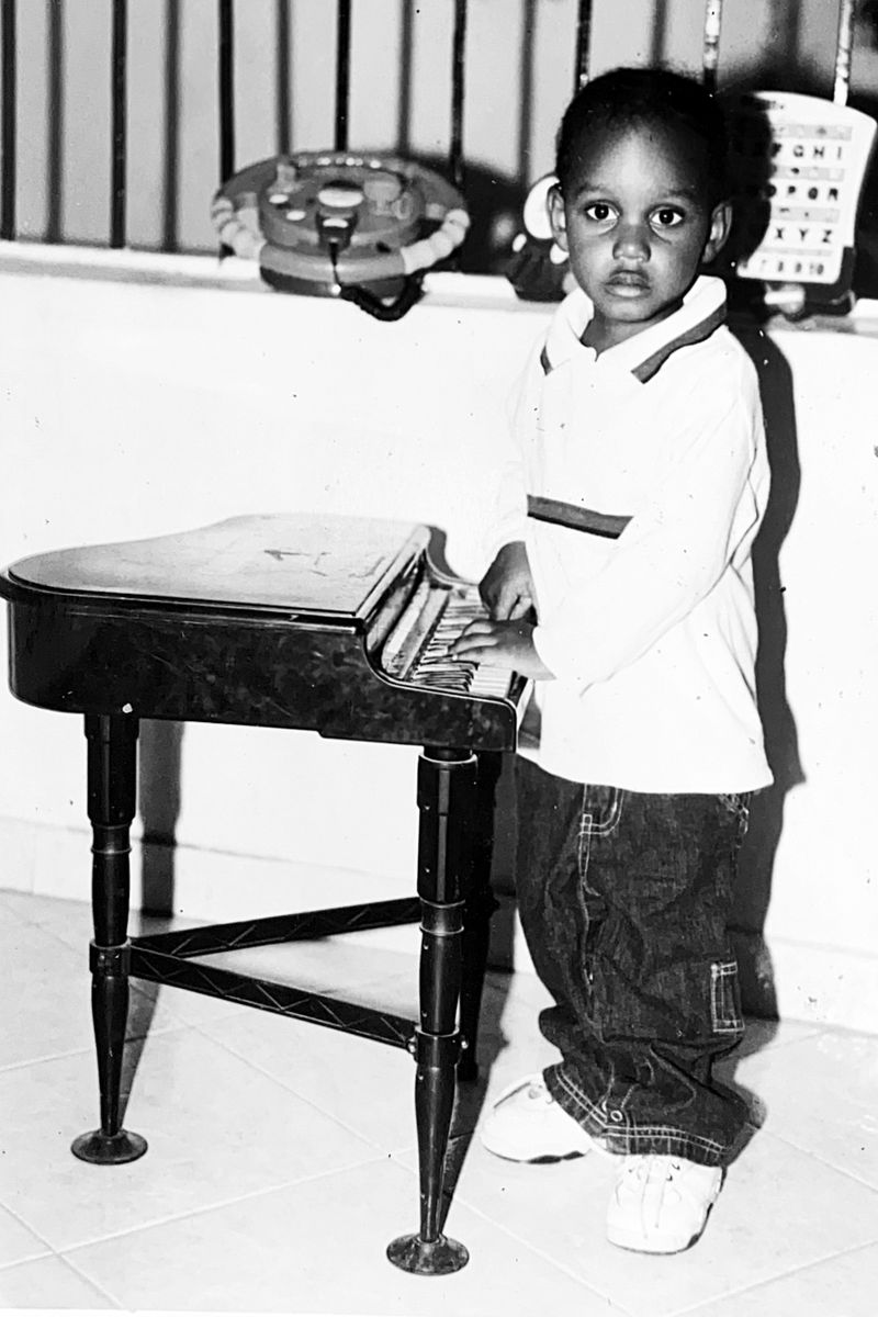 Roth$child as a small child, standing at a toy grand piano with both hands on the keys.